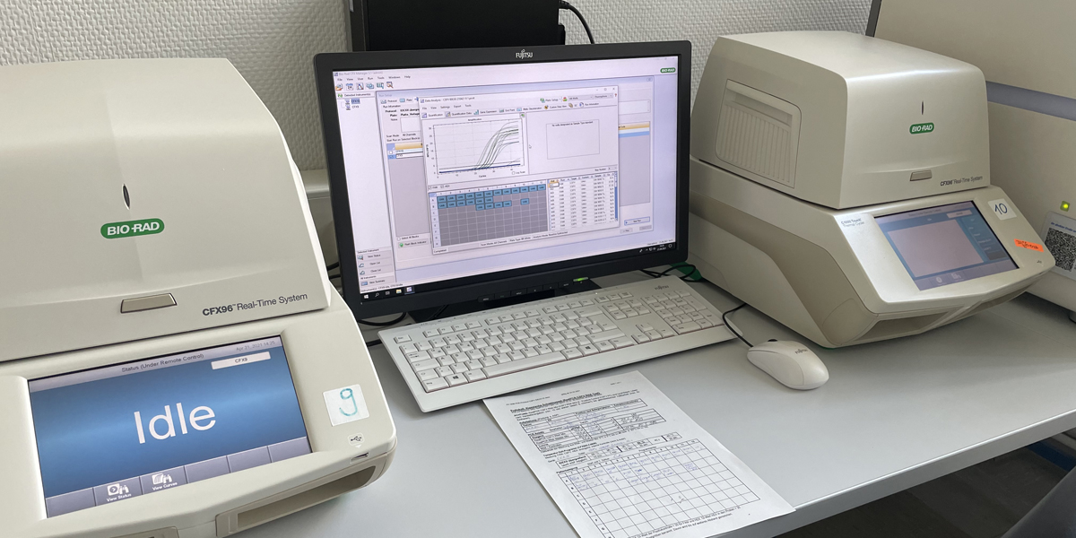 Bild: Auf einem Labortisch stehen zwei PCR-Geräte und ein Computer mit Bildschirm und Tastatur.