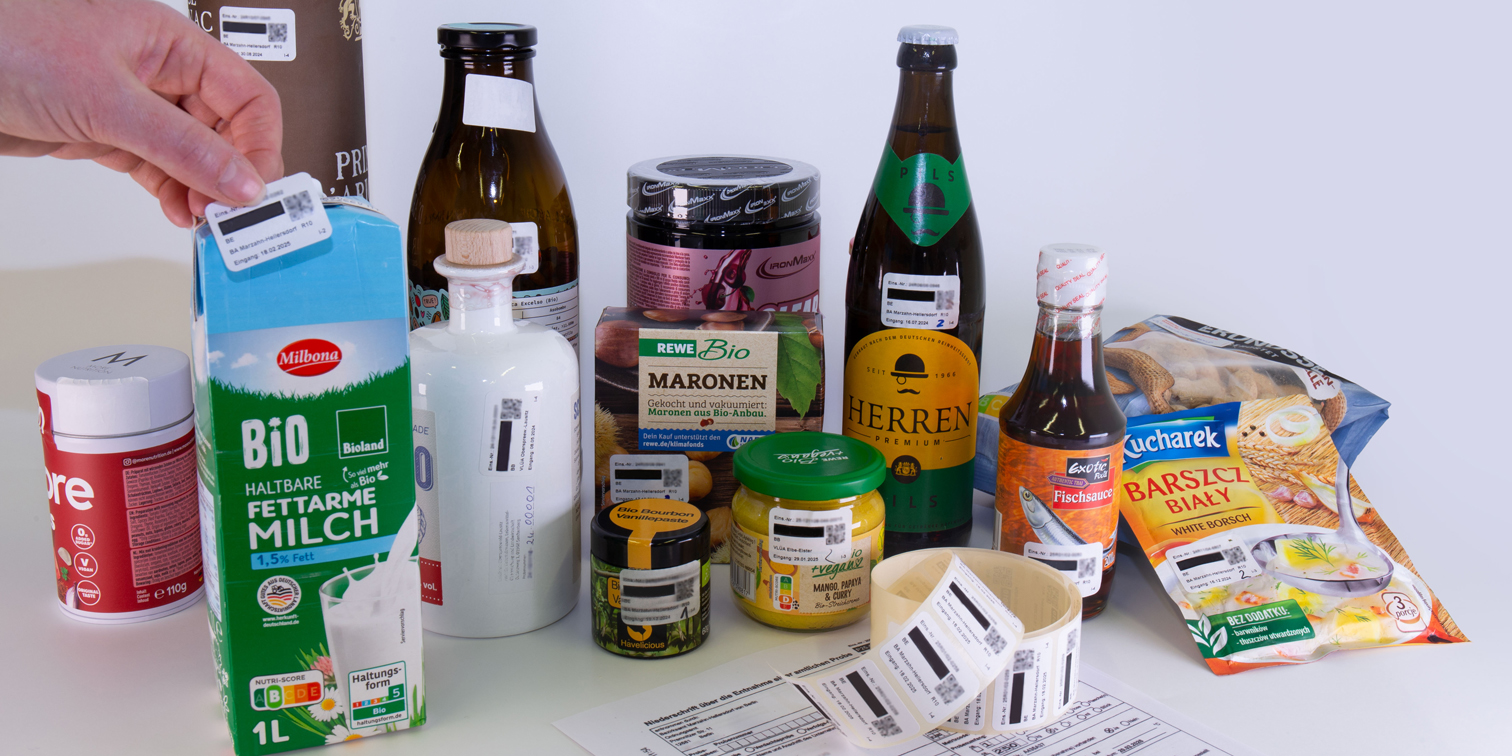 Bild: Verschiedene verpackte Lebensmittel, eine Hand klebt auf eine ein Etikett, Probeannahmeschein, Rolle mit ausgedruckten Etiketten